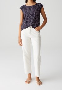 Haut à manches courtes bleu marine avec des pois roses et blancs, assorti à un jean blanc à jambes droites et des sandales de couleur claire.