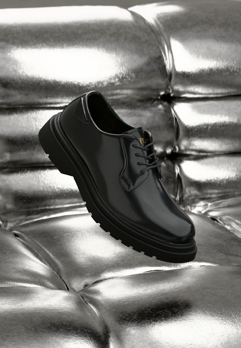 Black leather shoe with a glossy finish, rounded toe, thick black rubber sole, and contrasting laces. Narrow side cutout detail.