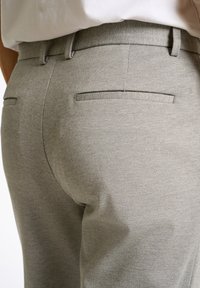 Grijze op maat gemaakte broek met een gladde textuur, slanke pasvorm en platte achterzakken. De tailleband is elastisch voor extra comfort.