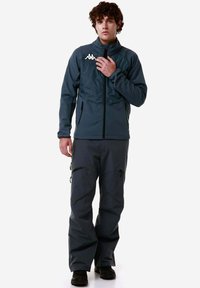 Giacca blu scuro con zip e petto imbottito, dotata di logo; abbinata a pantaloni larghi coordinati con tasche con zip e ginocchia rinforzate.