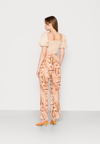 Conjunto de duas peças composto por uma blusa de mangas bufantes bege com as costas pregueadas e umas calças largas com padrão laranja. Mules de salto laranja completam o visual.