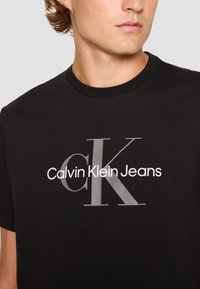 Camiseta de algodón negra con un destacado logo en blanco y gris: "Calvin Klein Jeans" sobre un "CK" estilizado. Diseño clásico de cuello redondo.