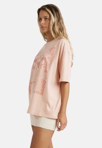 Lyserød bomulds t-shirt med korte ærmer, der har et stort grafisk design i koralfarver. Enkel, afslappet pasform og blød tekstur.