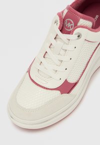 Λευκό αθλητικό παπούτσι με ροζ λεπτομέρειες, υλικά από δίχτυ και σουέντ, επίπεδα κορδόνια και κυκλικό λογότυπο στο πλάι. Σχεδιασμός χαμηλού προφίλ με υφή στην επιφάνεια.