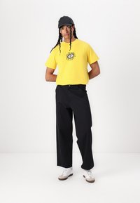 Kollane graafiline t-särk ringsusega kujundusega, millele on sobitatud mustad avarad püksid ja valged tossud hallide aktsentidega. Must kübar.