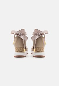 Beige nilkkaketjut, joissa on leveät satiininen nauhat, kudotut jute-akkentit ja valkoiset kumipohjat. Sileä pinta, minimalismin muotoilu.