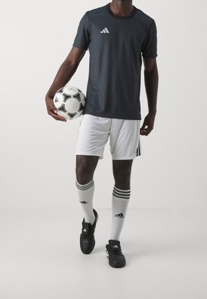 Zwart adidas T-shirt met korte mouwen en grijze accenten, gecombineerd met witte shorts en zwarte voetbalschoenen. Er wordt een voetbal in de rechterhand vastgehouden.