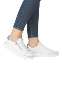 Baskets blanches avec un accent argenté au talon, dotées d'une fermeture éclair sur le côté, d'une semelle texturée, d'un design à lacets et d'un upper en cuir lisse.
