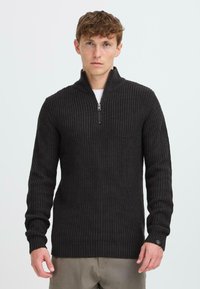 Donkergrijze sweater met rits en ribbelstructuur, lange mouwen en een iets losse pasvorm. Heeft een klein logo op de manchette.