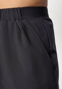 Shorts atléticos negros con una cinturilla elástica, que presentan una textura de tela suave y bolsillos laterales. El diseño es streamlined y funcional.