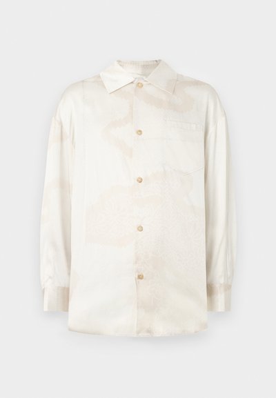 Camisa de manga larga color beige claro en tejido sedoso con un sutil patrón floral, cuenta con un cierre frontal de botones y un bolsillo en el pecho.