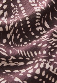 Textil med en mörk lila bakgrund och vita abstrakta mönster som liknar blad och prickar, med en mjuk, något strukturerad yta.