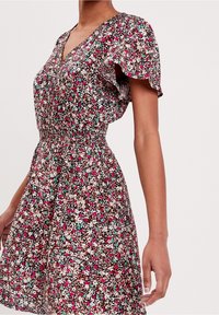 Robe fleurie avec manches courtes à volants, présentant des fleurs multicolores sur un fond marron. Taille élastique avec une silhouette fluide.