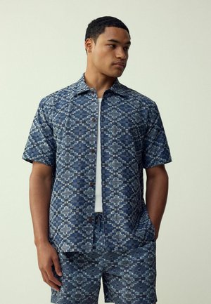 Kurzarmhemd in Blautönen mit geometrischen Mustern,Knopfverschluss und lässiger Passform. Kombiniert mit passenden Shorts für einen stimmigen Look.