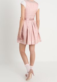 Abito rosa con corpetto aderente e gonna svasata, caratterizzato da un motivo testurizzato e decorazioni in nastro di raso. Abbinato a maniche bianche e tacchi rosa.