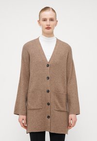 Hnědý pletený kardigan s výstřihem do V, dlouhými rukávy, pěti černými knoflíky a dvěma předními kapsami. Měkká textura a uvolněný střih.