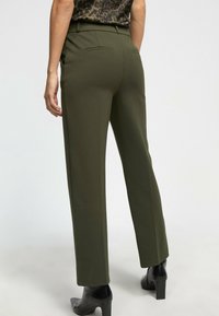 Pantalones ajustados verde oliva con un diseño de pierna recta, textura suave, presillas para cinturón y dos bolsillos traseros, combinados con botas negras de tacón.