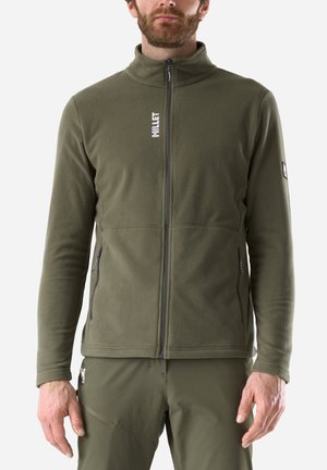 Mann trägt olivgrüne Fleecejacke mit Reißverschluss und Seitentaschen sowie passende Hose, steht vor einfarbigem Hintergrund.