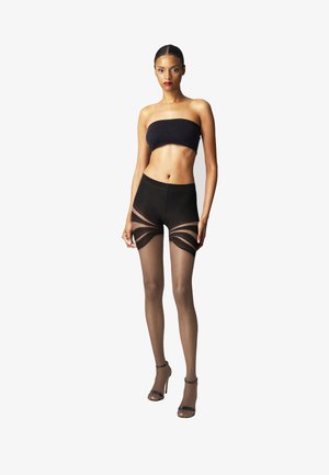 Schwarzer Bandeau-Top, hochgeschnittene Shorts mit durchscheinenden Einsätzen und durchsichtigen Strumpfhosen. Model trägt offene High Heels. Sauberes, minimalistisches Design.
