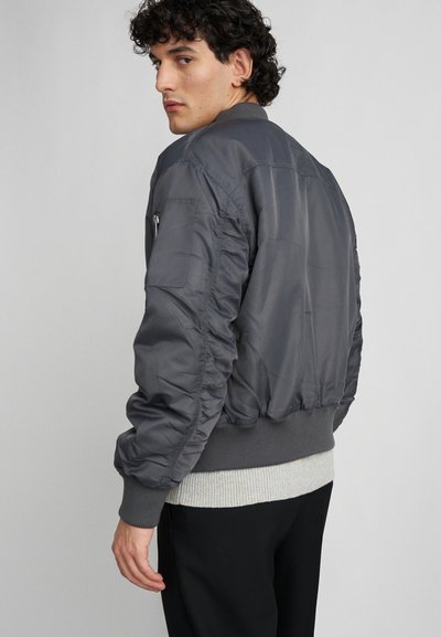 Grijze bomberjack met ribgebreide manchetten en zoom; heeft gatherende texturen op de mouwen en een zijzak met ritsdetail.