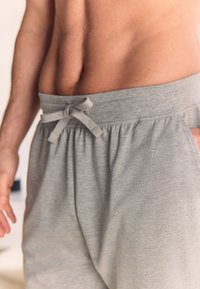Pantaloncini grigi con coulisse realizzati in tessuto morbido, dotati di una cintura elastica con un fiocco decorativo e tasche laterali.