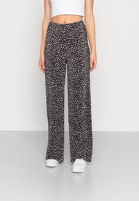 Pantalon noir à jambes larges avec un petit motif floral blanc, en tissu léger, doté d'une taille élastique. Assorti à des baskets blanches.