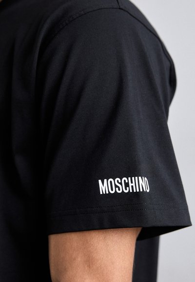 T-shirt en coton noir avec un logo "Moschino" blanc sur la manche. Texture lisse, design décontracté, manches courtes et col rond.