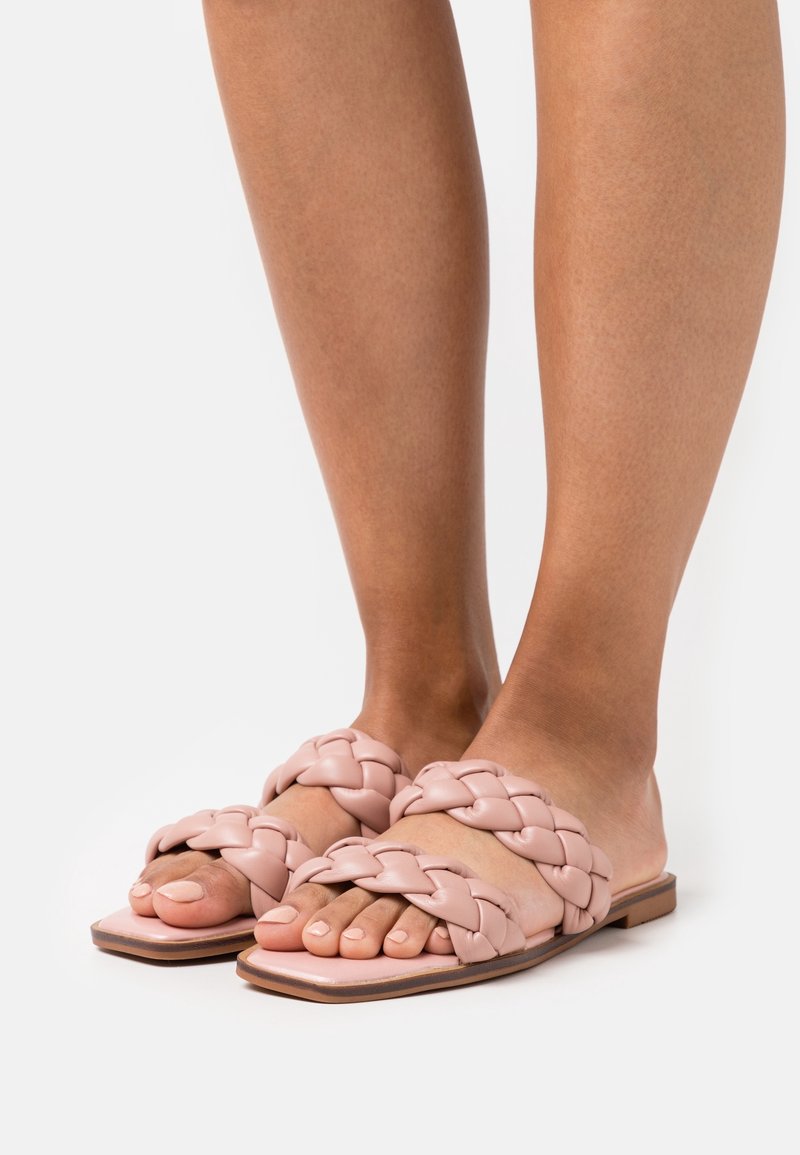 Flätade slidesandaler gjorda av mjukt rosa läder med en platt sula, med en slät yta och design med öppen tå.