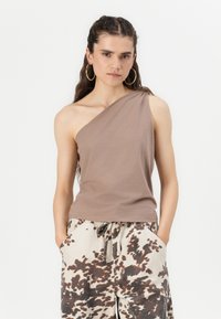 Top maro, cu un singur umăr, dintr-un material moale, asortat cu pantaloni bej cu model, având stropi maronii. Prezentat pe un model cu păr ondulat.