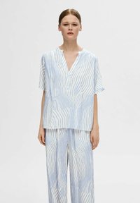 Blusa azzurro chiaro e bianca con motivo, maniche corte, scollo a V e vestibilità morbida, abbinata a pantaloni larghi coordinati con lo stesso design.