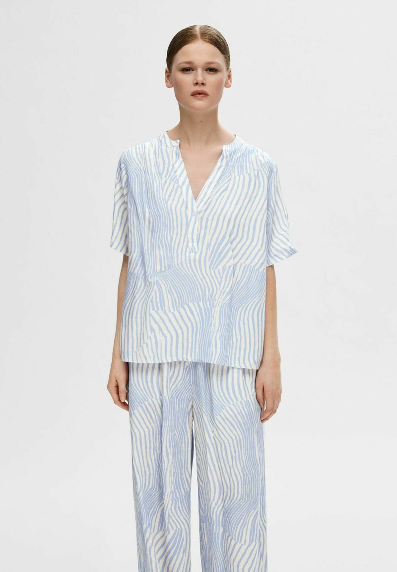 Blusa azzurro chiaro e bianca con motivo, maniche corte, scollo a V e vestibilità morbida, abbinata a pantaloni larghi coordinati con lo stesso design.