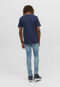En marineblå bomulls t-skjorte med korte ermer, kombinert med lyseblå tettsittende jeans og marineblå høy-top sneakers, sett fra baksiden.