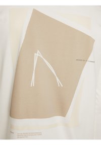 Weißes T-Shirt mit abstrakten beigen geometrischen Formen und einem texturierten Netzbereich mit weißen Linien, ergänzt durch einen Drucktext.