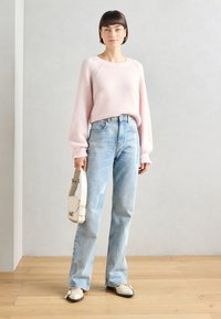 Light pink knitted sweater with ribbed texture, loose sleeves; faded blue high-waisted jeans; cream handbag with adjustable strap; black and cream flats.