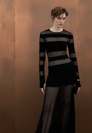 Svart genomskinlig klänning med långa ärmar, med horisontella randmönster i ogenomskinligt och transparent tyg, slutar ovanför ankeln.