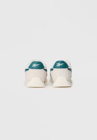 Un paio di sneakers Reebok bianche e turchesi viste da dietro su uno sfondo bianco uniforme.
