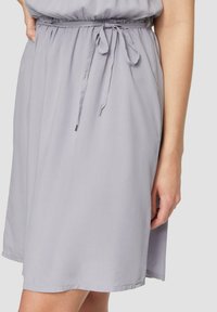 Hellgraues Kleid aus weichem Stoff, mit elastischem Bund und einem Bindegürtel. Der Saum ist leicht gewellt und hat einen dezenten Glanz.