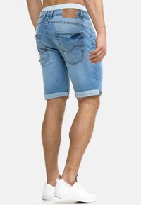 Pantaloni corti in denim blu chiaro con risvolti, dotati di due tasche posteriori e un'etichetta del marchio visibile sulla vita.