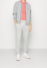 Grå bomberjacka, rosa polo skjorta, ljusgrå sweatpants och vita sneakers. Avslappnad outfit med öppen dragkedja på jackan och snörning på byxorna.