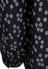 Tessuto nero con un motivo floreale bianco e forme a diamante. Il materiale ha una consistenza morbida, e il design è distribuito in modo uniforme.
