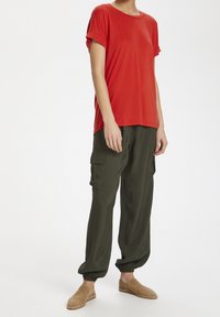 Red short-sleeve t-shirt paired with olive green cargo pants featuring side pockets and elastic cuffs; worn with tan slip-on shoes.
