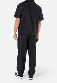 Zwarte shirt met korte mouwen en bijpassende broeken, met een geribbelde textuur en een relaxte pasvorm. De outfit is ontworpen voor casual gebruik.