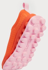 Sapatilha tricotada laranja com sola de borracha rosa, com solas arredondadas, um laço na parte de trás e um design sem emendas para maior conforto.