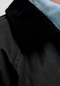 Czarna skórzana kurtka z kołnierzem z sztruksu, o gładkiej fakturze i kontrastowej jasnoniebieskiej podszewce. Zbliżenie podkreśla detale tkaniny.