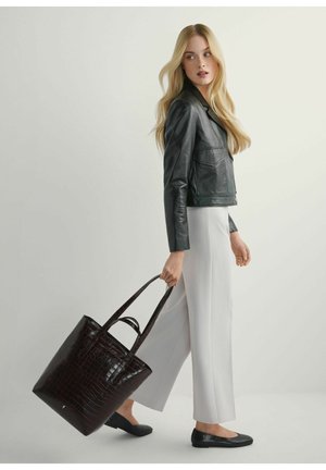 Blondynka w czarnej skórzanej kurtce, białe szerokie spodnie, czarne baleriny, nosi dużą ciemnobrązową torbę z tłoczonym wzorem skóry krokodyla.