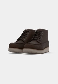 Brown suede ankle boots feature a rounded toe, contrasting lighter sole, six eyelet lace-up design, and stitching details along the edges.
