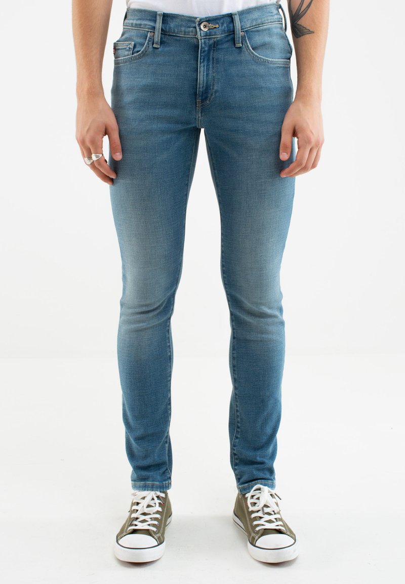 Slim-fit, svetlo modri jeansi iz denima z izbledelim učinkom, kontrastnim šivom, petimi žepi ter gumbom in zadrgo. Obuti so z zelenimi supergami.