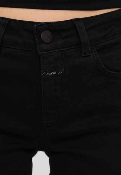 Svarte denimbukser med knappeåpning og en etikett som leser "CLOSED." Har en glatt tekstur og en tettsittende design.
