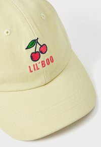 Sárga pamut sapka hímzett cseresznyékkel és rózsaszín "LIL' BOO" szöveggel. Ívelt csúccsal rendelkezik, és látható varrási részletei vannak.