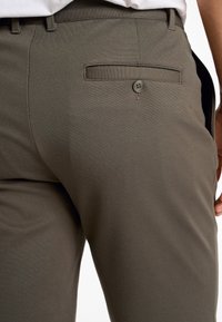 Donker olijfgroene broek van een gladde, gestructureerde stof. Voorzien van een achterzak met knoopsluiting. Netjes gesneden pasvorm met ri loop.